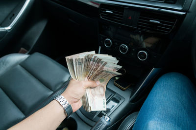 Cropped hand of man holding paper currency in car