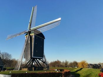 Traditional windmill on field against clear blue sky