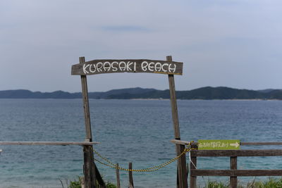 Information sign by sea against sky