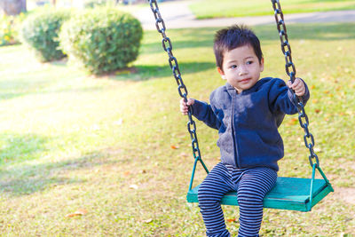 Cute boy sitting on swing in playground