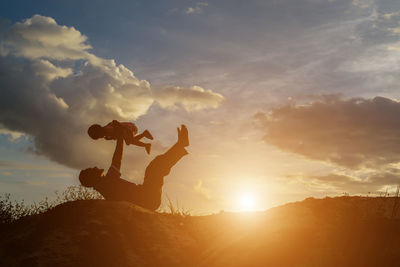 Silhouette man holding sun against sky during sunset