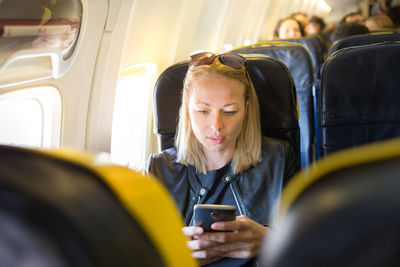 Mid adult woman using smart phone while sitting at airplane