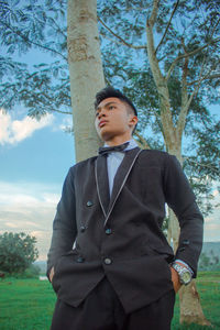 Young man looking away while standing on tree trunk