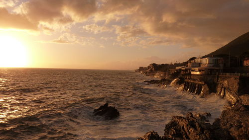 Waves splashing on rocks at shore against sky