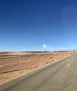 Road amidst field against clear blue sky