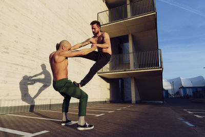 Young athletic shirtless men doing an urban workout outdoors practicing balance exercises