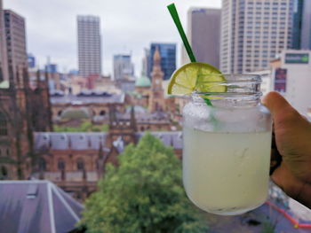 Cropped hand holding drink against cityscape