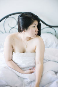 Young woman looking away while sitting on bed