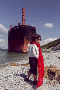 Fashionable boy child with long hair dance next to a large ship that ran aground near novorossiysk