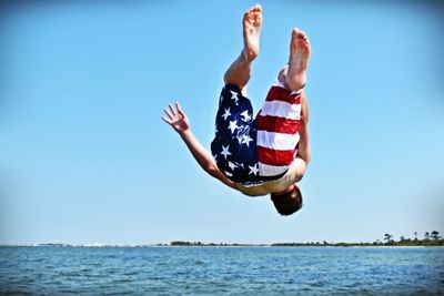 Full length of shirtless man backflipping at beach against clear sky