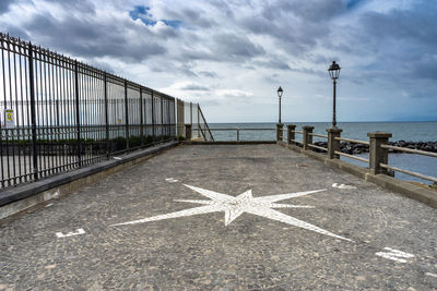 Arrow symbol on railing by sea against sky