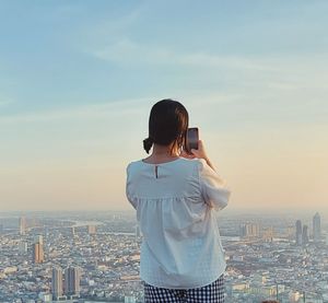 Rear view of woman photographing sea against sky during sunset