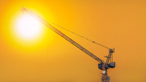 Low angle view of crane against orange sky
