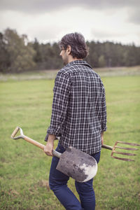 Rear view of man with gardening tools walking on organic farm