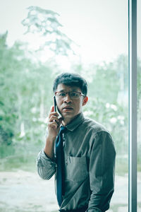 Young man using mobile phone while standing on window