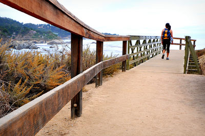 Man walking on footbridge against sky