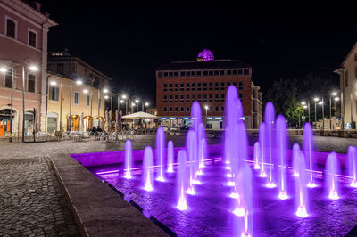 Illuminated fountain against building at night