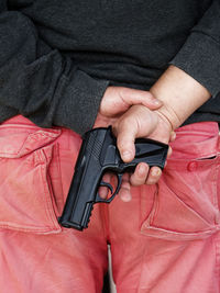 Midsection of man holding gun behind back