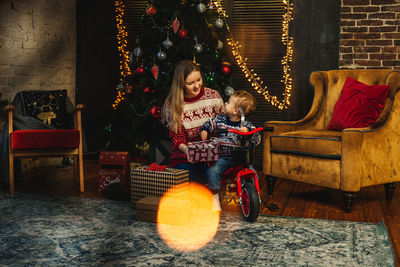 Smiling mother with son sitting against illuminated christmas tree at home