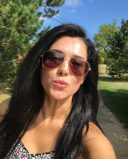 Close-up portrait of young woman in sunglasses against trees