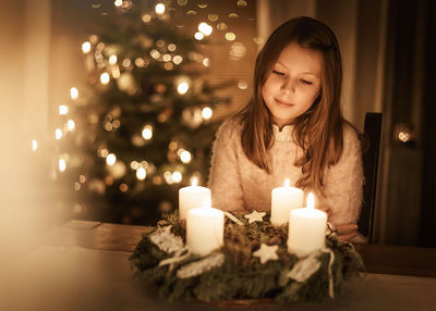 Child sits alone in front of a glowing advent wreath and looks forward to christmas