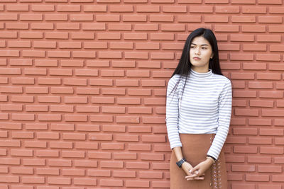 Young woman standing by brick wall