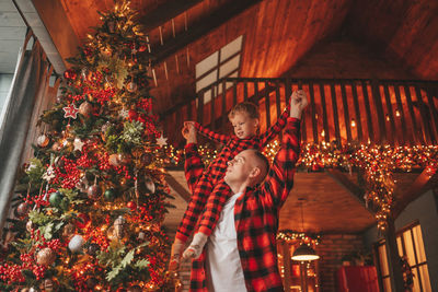 Candid authentic happy dad and son in red plaid pajamas fooling around at wood lodge xmas decorated