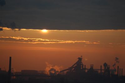 Silhouette of factory against sky during sunset