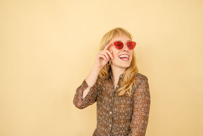 Happy young woman wearing sunglasses while standing against yellow background