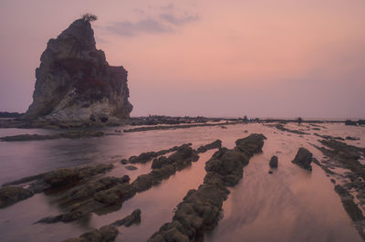 Rock formation on beach against sky during sunset