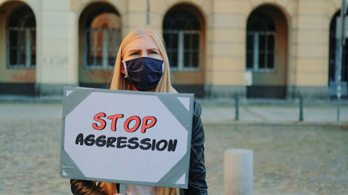 Portrait of person holding sign against building in city