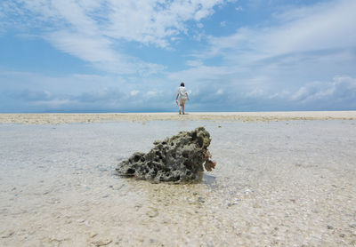 Low angle view of woman walking at beach against cloudy sky on sunny day