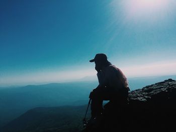 Silhouette man sitting on mountain against sky