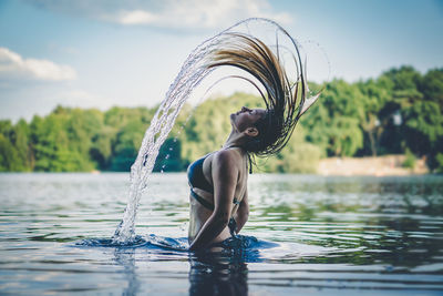 Side view of young woman tossing hair in lake 