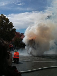 Firefighters extinguishing fire on street against sky