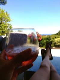 Low section of woman holding beer glass against clear blue sky