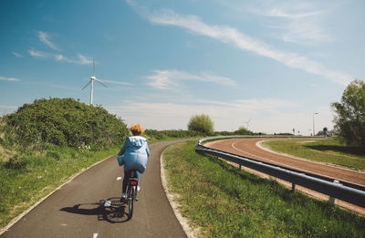 Rear view of woman riding bicycle on road during sunny day