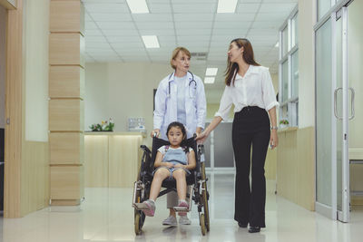 While the doctor comes to see her, a young asian girl patient smiles in her wheelchair.