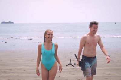 Full length of young woman walking on beach against clear sky