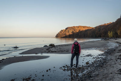 Woman standing on rock by sea against clear sky