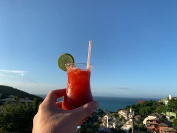 Midsection of person holding drink against blue sky