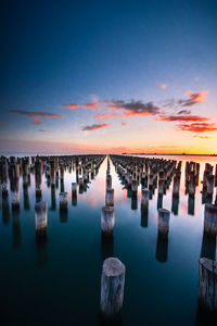 Wooden posts in sea against sky at sunset