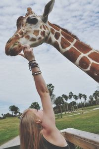 Woman reaching giraffe against sky