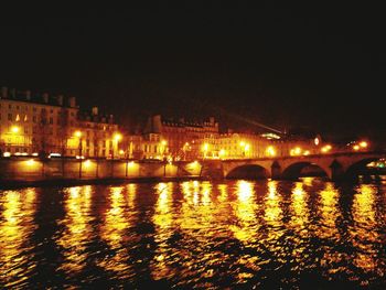 Illuminated city by river against sky at night