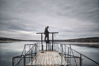 Man standing on pier over lake against sky