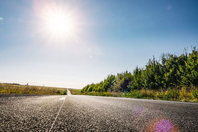 Road by trees against sky on sunny day