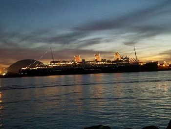 Illuminated commercial dock by sea against sky at night