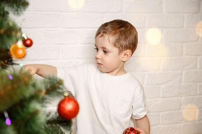 Cute boy decorating christmas tree against wall