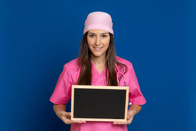 Portrait of smiling woman with blackboard standing against blue background