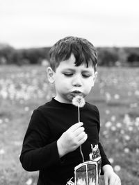 Boy blowing dandelion standing against field